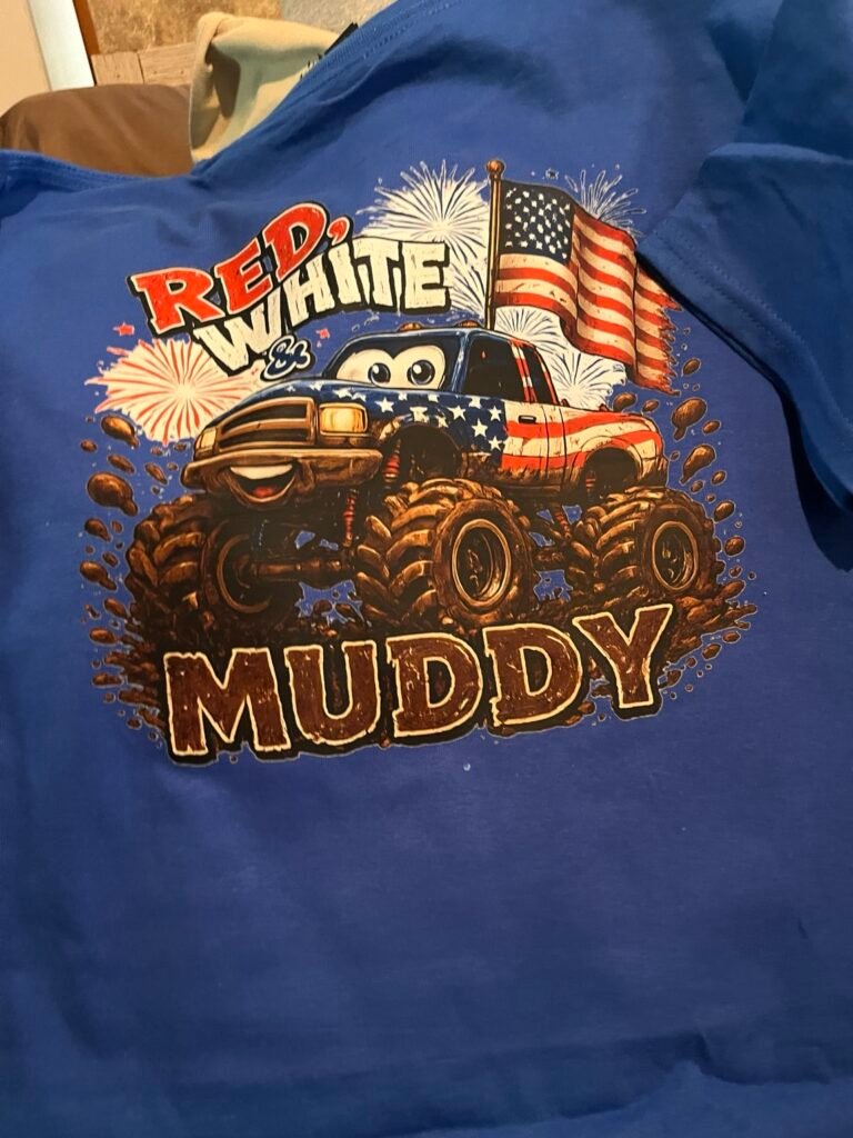 Youth royal blue patriotic monster truck T-shirt featuring a red, white and blue muddy truck, American flag, fireworks, and “Red, White & Muddy” design.